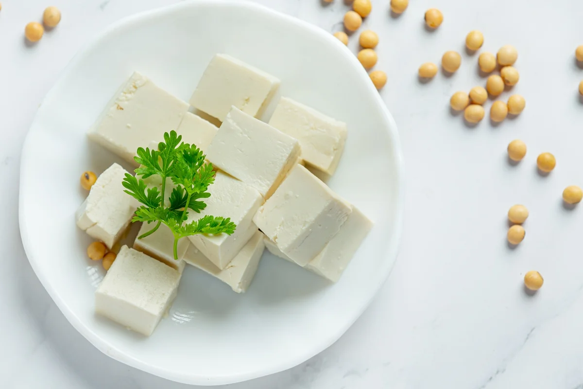 Foto colorida com fundo branco com algumas sementes espalhadas, um prato branco com vários cubos de tofu no centro - Metrópoles.