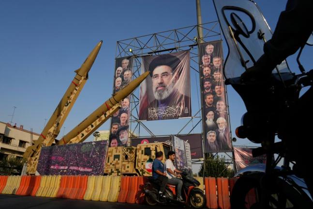 Motorbikes drive past Iranian missiles and banners showing portraits of the Iranian Supreme Leader Ayatollah Mojtaba Khamenei and the late armed forces commanders and nuclear scientists, who were killed in Israeli and US strikes, displayed in a military ex