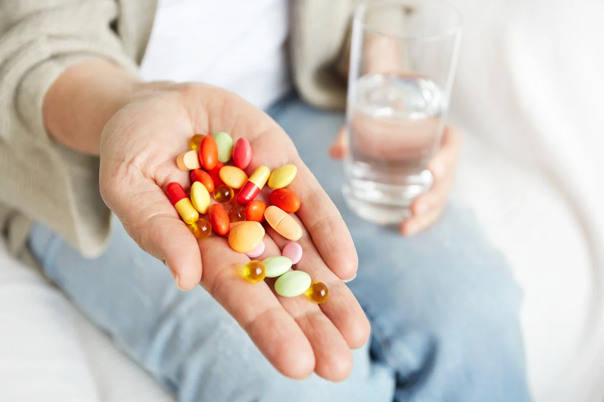 Close up das mãos de uma pessoa segurando e mostrando vários medicamentos coloridos e antibióticos. Conceito de vitaminas. Metrópoles
