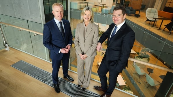 Two men in suits and a woman stand for a photo in an office building