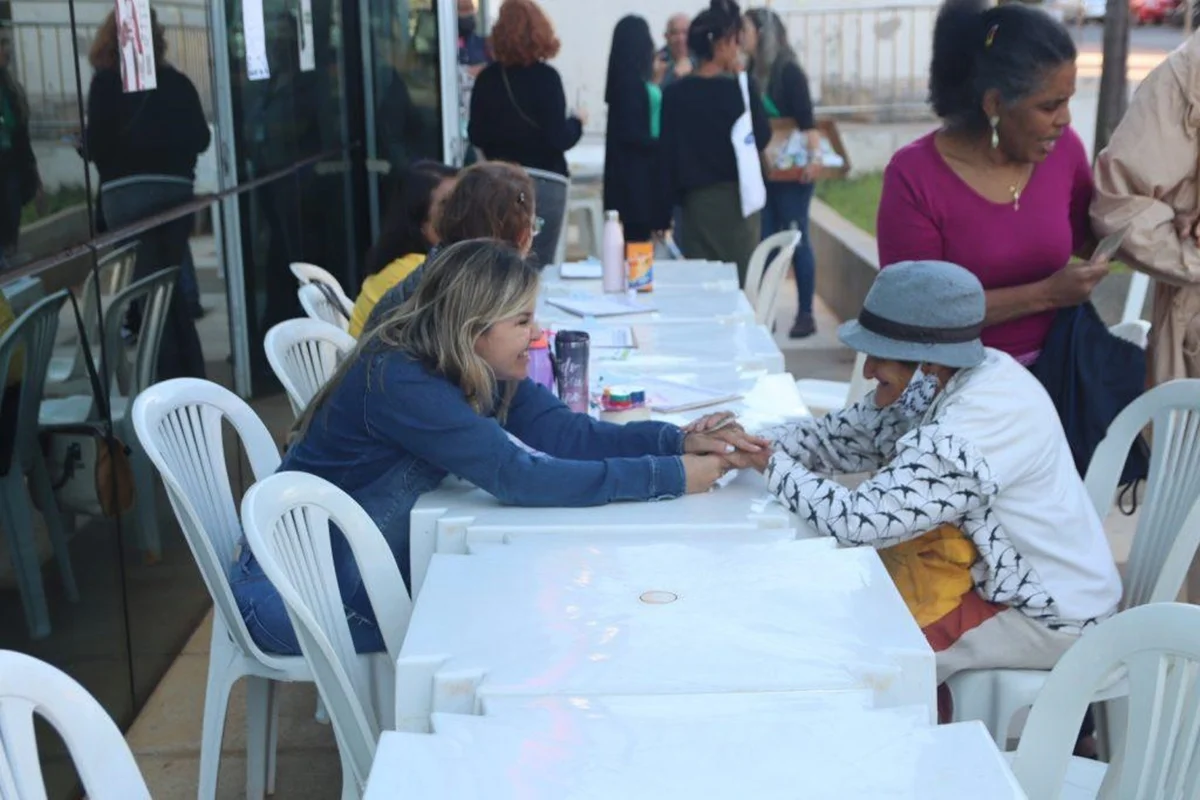Imagem colorida de duas mulheres sentadas frente a frente, separadas por uma mesa branca