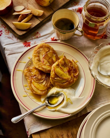 Three apple pancakes on a plate with yoghurt and honey, beside coffee and sliced apples