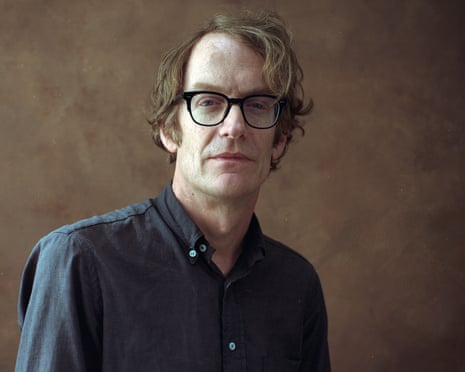 Author Patrick deWitt, with wavy hair and glasses, looks at the camera